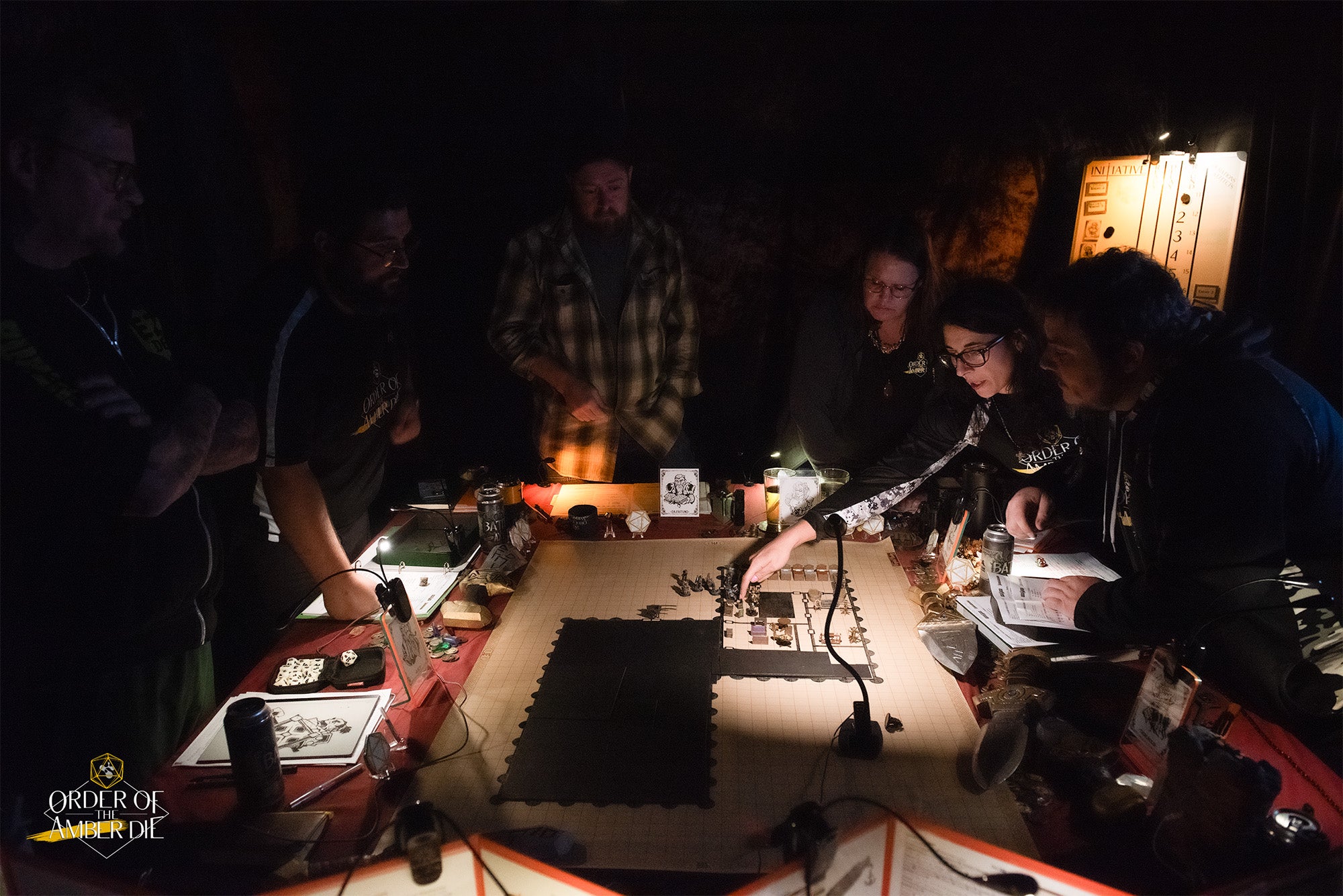 A group of pathfinder players gathered around a a lowly lit gaming table covered in character sheets, maps, and dice.