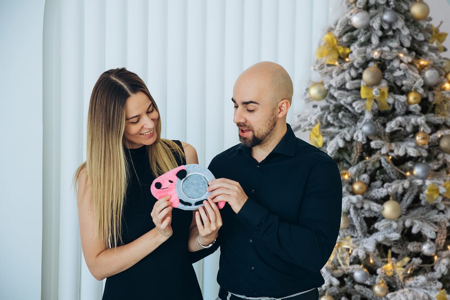 A couple by a Christmas tree looking at a handmade opossum dice tray they got as a gift