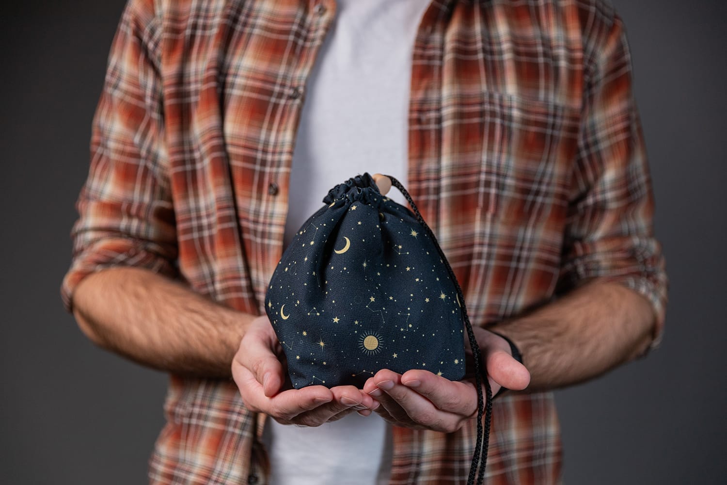 Handmade drawstring dice bag with a navy night sky print, gold moons and constellations, held in two hands
